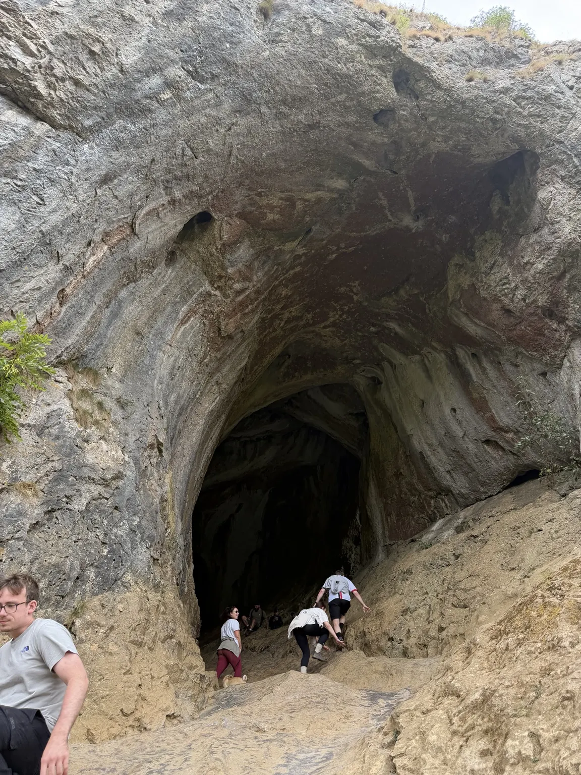The huge limestone entrance to Thor's Cave with walkers climbing inside
